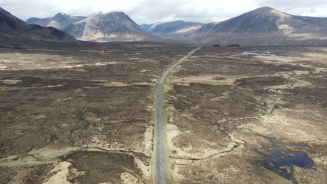 Impresionante-Vista-Aérea-De-La-Carretera-En-Un-Terreno-Accidentado-Del-Desierto-De-Las-Tierras-Altas-Escocesas