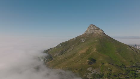 lions head mountain rising from fog. aerial descending shot of steep slopes and rock peak. cape town, south africa