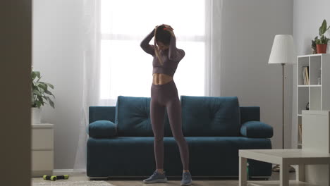 young sexy woman is warming body before training at home moving head to sides standing in living room sport activity and healthy lifestyle