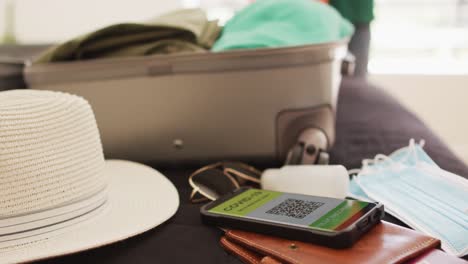 maletas de vacaciones con máscaras y gel de desinfección, teléfono inteligente con pasaporte de vacuna contra la covid 19