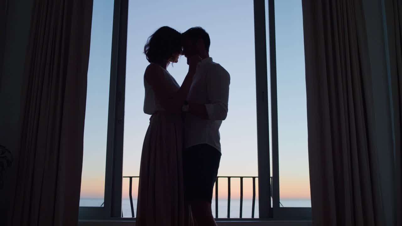 해가 지는 날 호텔 방에서 춤을 추는 행복한 커플의 실루 ⁇  신혼여행을 즐기고 아름다운 바다 전망으로 휴가를 즐기고 있습니다.