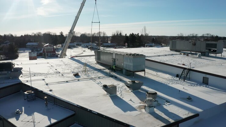 Luftfoto af faglærte arbejdere, der installerer ny HVAC-enhed på industribygning