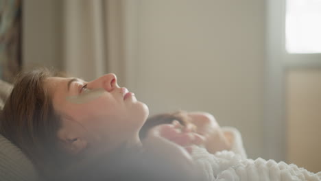 young female puts head on pillow straightening hair with hands. woman with patches under eyes rests on soft pillow in light room slow motion