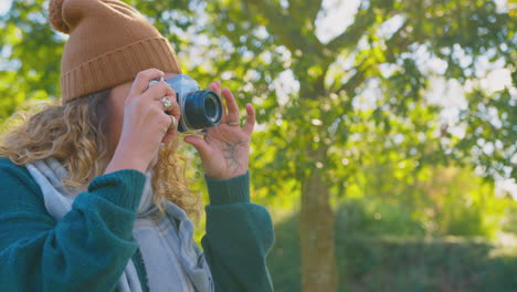 woman in autumn countryside taking photo on retro style digital camera to post to social media