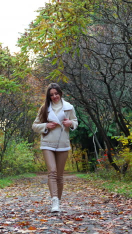 caucasian lady with long dark hair having a walk in the autumn forest. smiling woman kick the leaves on the ground with her foot. vertical video