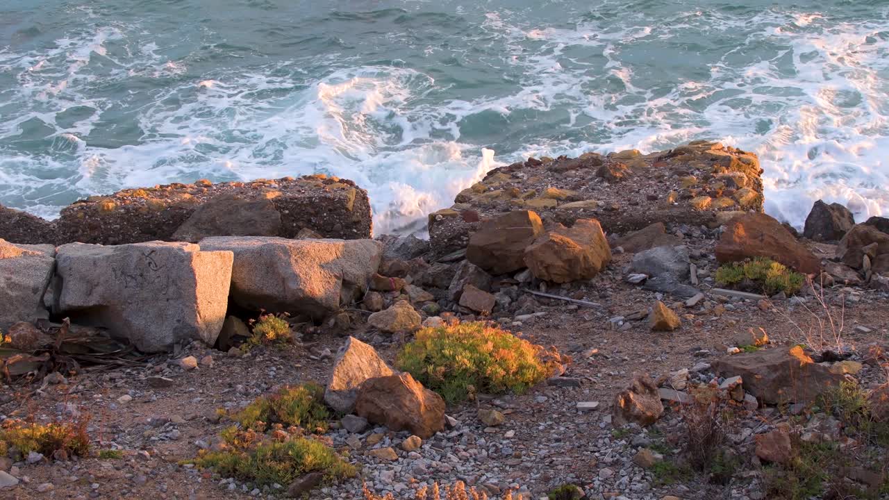 Havbølger rammer blidt klipperne ved siden af en grusvej ved solnedgang