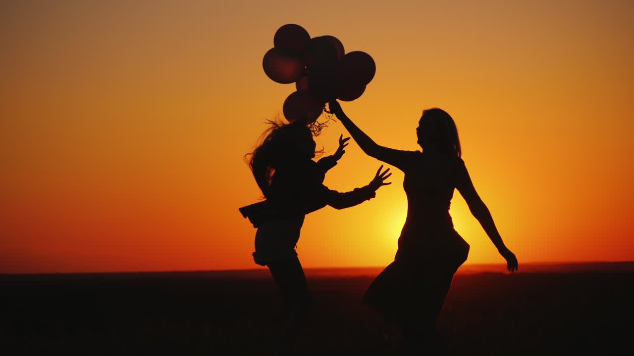 mamá e hija se divierten al atardecer bailando y sosteniendo globos