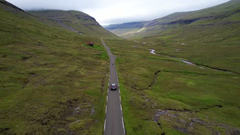 Faroese-sheeps-cross-street-while-car-drives-along-one-lane-road-in-Saksun,-Faroe-Islands