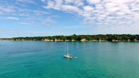 antena ascendente de velero anclado en agua azul con fondo de isla selvática