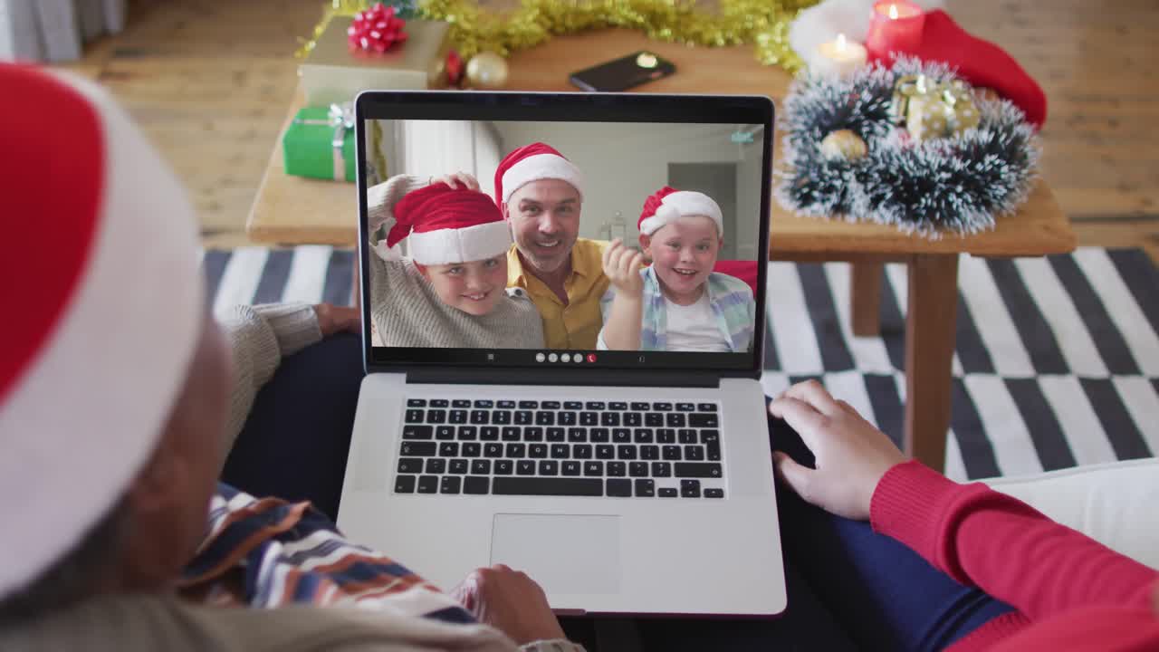 madre y hija afroamericanas usando una computadora portátil para una videollamada de navidad con la familia en la pantalla