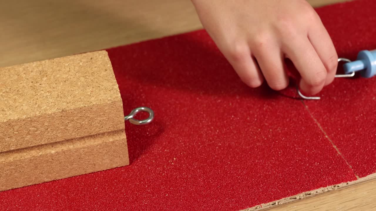 A hand uses a spring scale to measure friction on a wooden block over sandpaper, demonstrating force and resistance