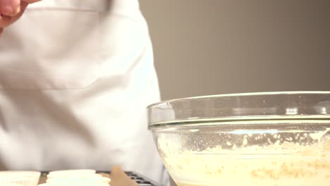 pastry maker passing cupcake mix to molds from bowl with scoop and spoon