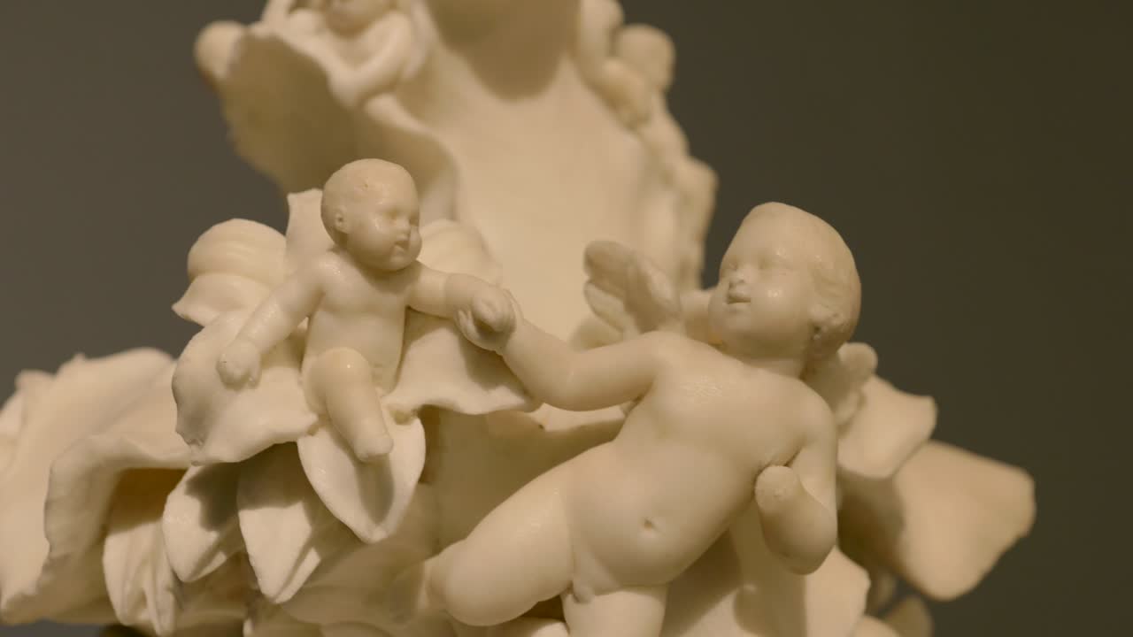 Close up of an ivory cherub statue sitting on a flower and holding another cherub's hand