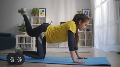 joven mujer deportiva está entrenando en casa de pie en palmas y rodillas levantando la pierna hacia arriba entrenando la parte trasera de las caderas fitness y gimnasia en el apartamento