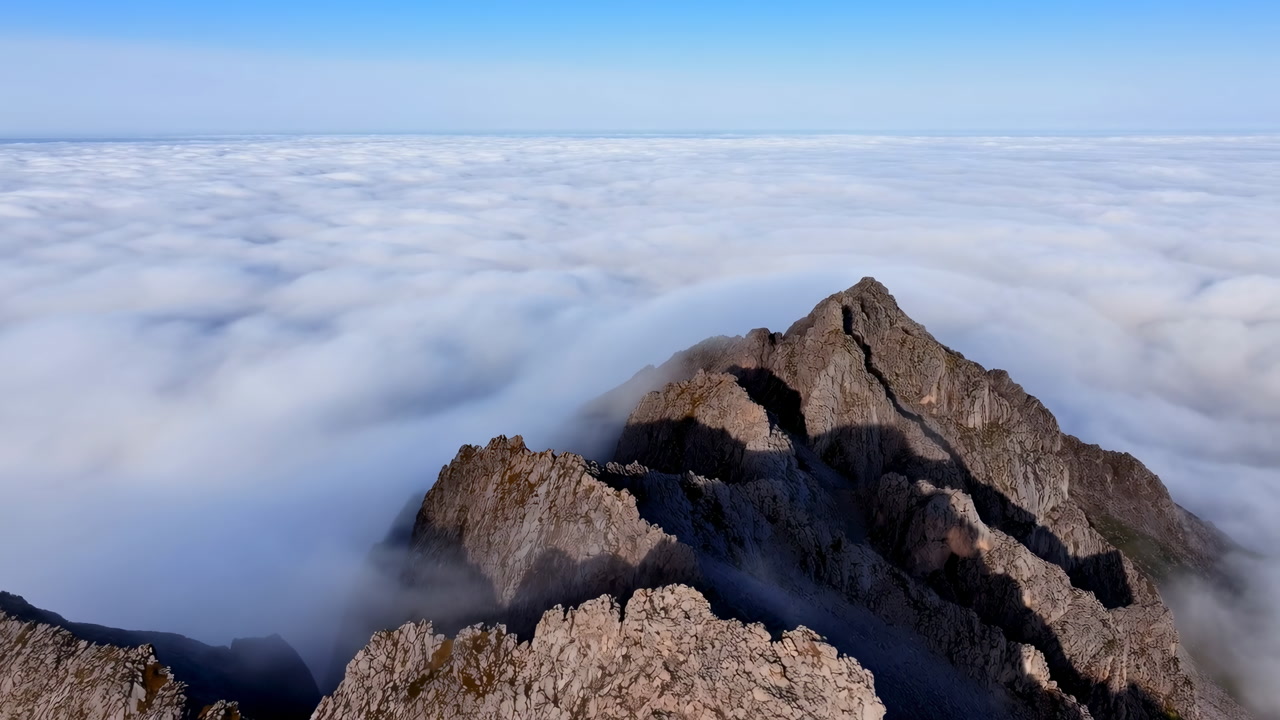 Aerial Mountain Peak Above Clouds, Cinematic Drone Perspective Over Rugged Rock Ridges, Soft Cloud Inversion