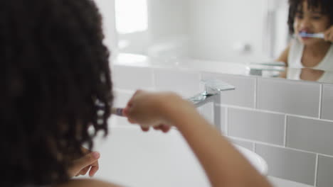 Biracial-boy-brushes-teeth-in-a-bright-bathroom