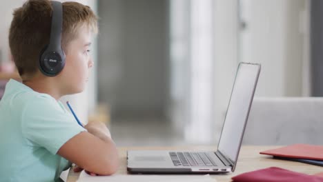 Happy-caucasian-boy-sitting-at-table-and-using-laptop-for-online-lesson,-slow-motion