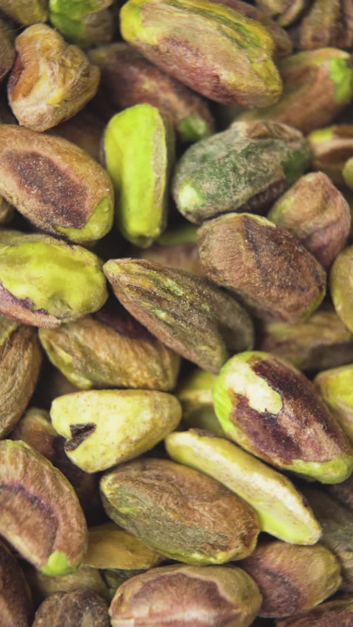 Vertical macro footage highlighting the textures and natural tones of shelled pistachios. Ideal for healthy food, snacks, or ingredient-focused backgrounds