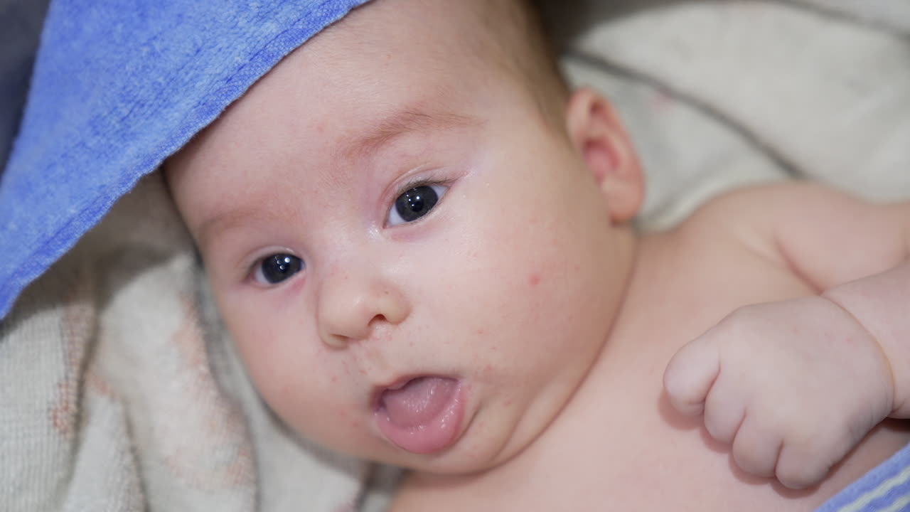 Calm little infant in towel resting after the bathing time. Peaceful baby boy looking straight into camera. Close up.