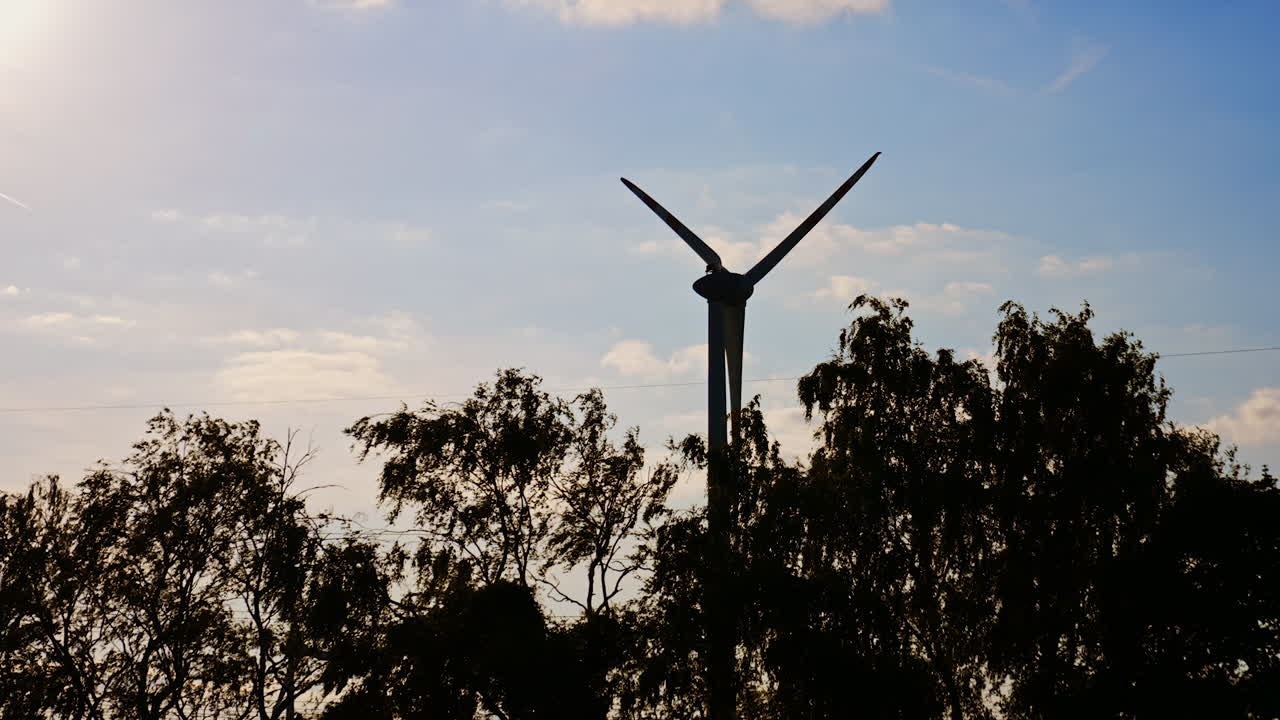 Turbine rises at sunset. A wind turbine silhouetted by the warm glow of sunset and surrounded by trees on a calm evening