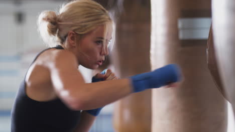 female boxer in gym training with old fashioned leather punch bag