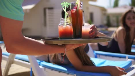 un camarero irreconocible que trae cócteles para hermosas chicas jóvenes que se relajan junto a la piscina. fiesta en la piscina de verano. toma en cámara lenta