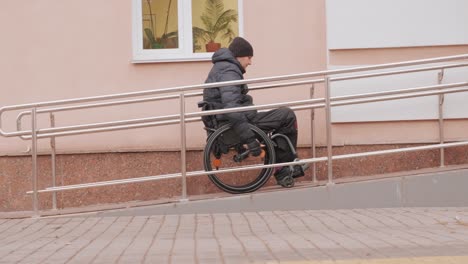 a person with a disability moves along the street in a wheelchair, climbs the ramp