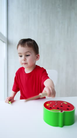 toddler boy wearing red t-shirt stands at the desk. little plays with an educational toy at home. vertical video.