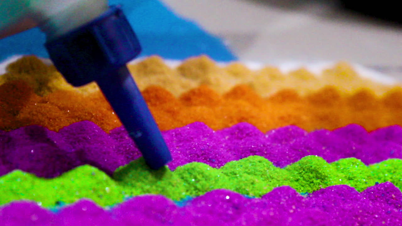 Rangoli patterns emerge with glue drawing on multicolored powders in blue, orange, yellow, red, purple, green. Traditional Indian art, festive Diwali spirit with sparkling layers and creative designs