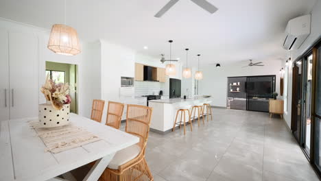 moderna cocina de casa tropical de lujo con asientos bronceados alrededor de encimera y mesa blancas, retroceso