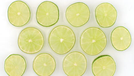 water splashes in slow motion. top view: several lime circles washed by water on a white background. chopped fruit.