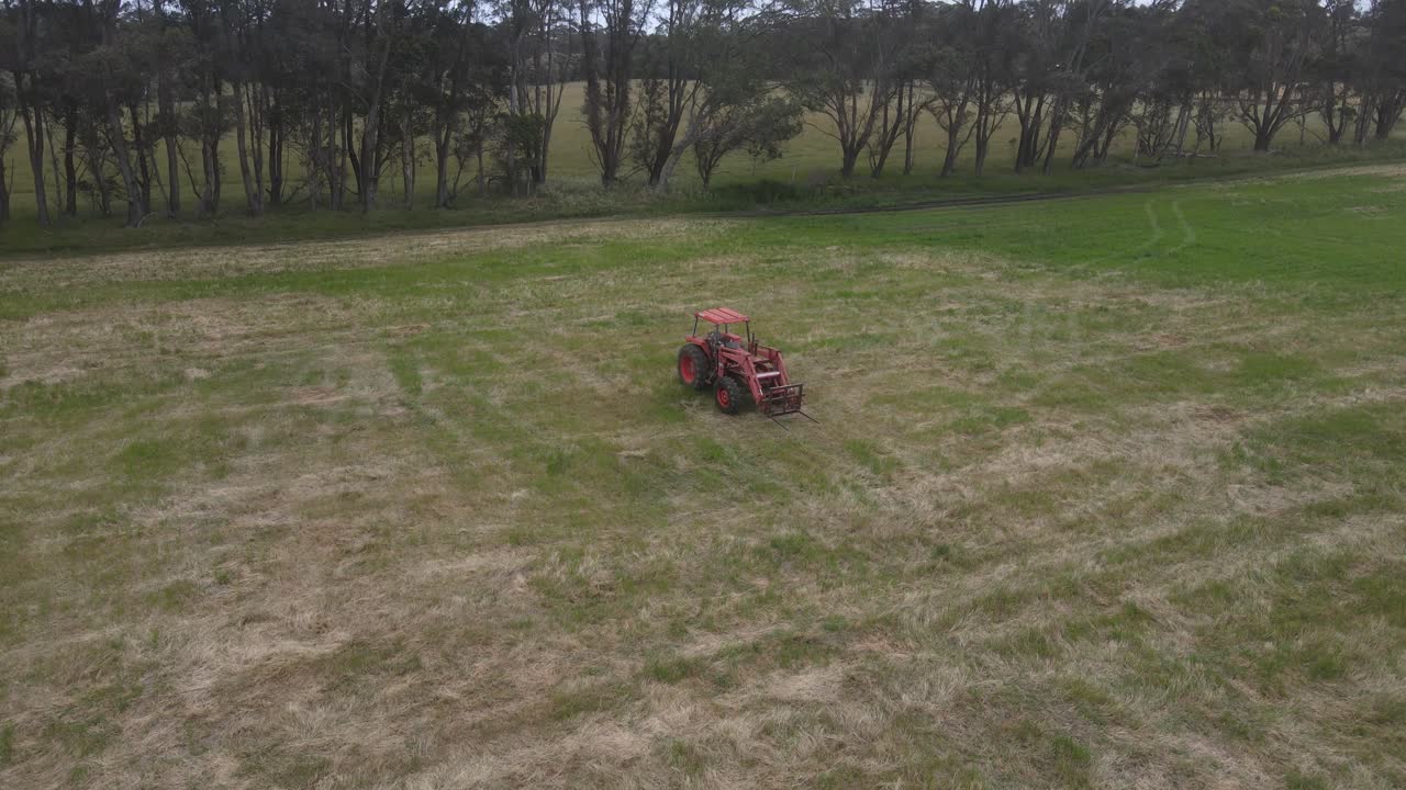 낮 시간에 농업 분야의 풀밭에 주차된 빨간 트랙터를 보여주는 공중 궤도