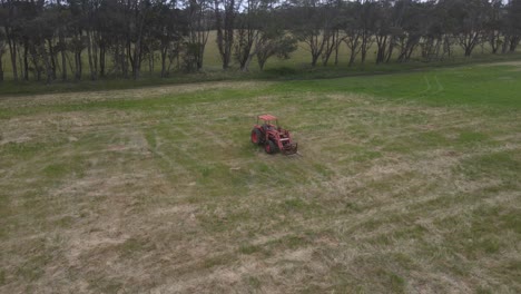 órbita aérea que muestra un tractor rojo estacionado en la hierba del campo agrícola durante el día