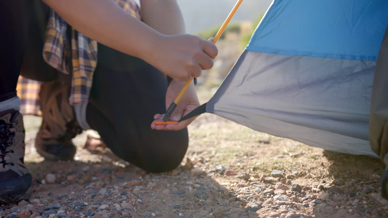 Setting up tent, woman securing tent pole during mountain hike camping trip