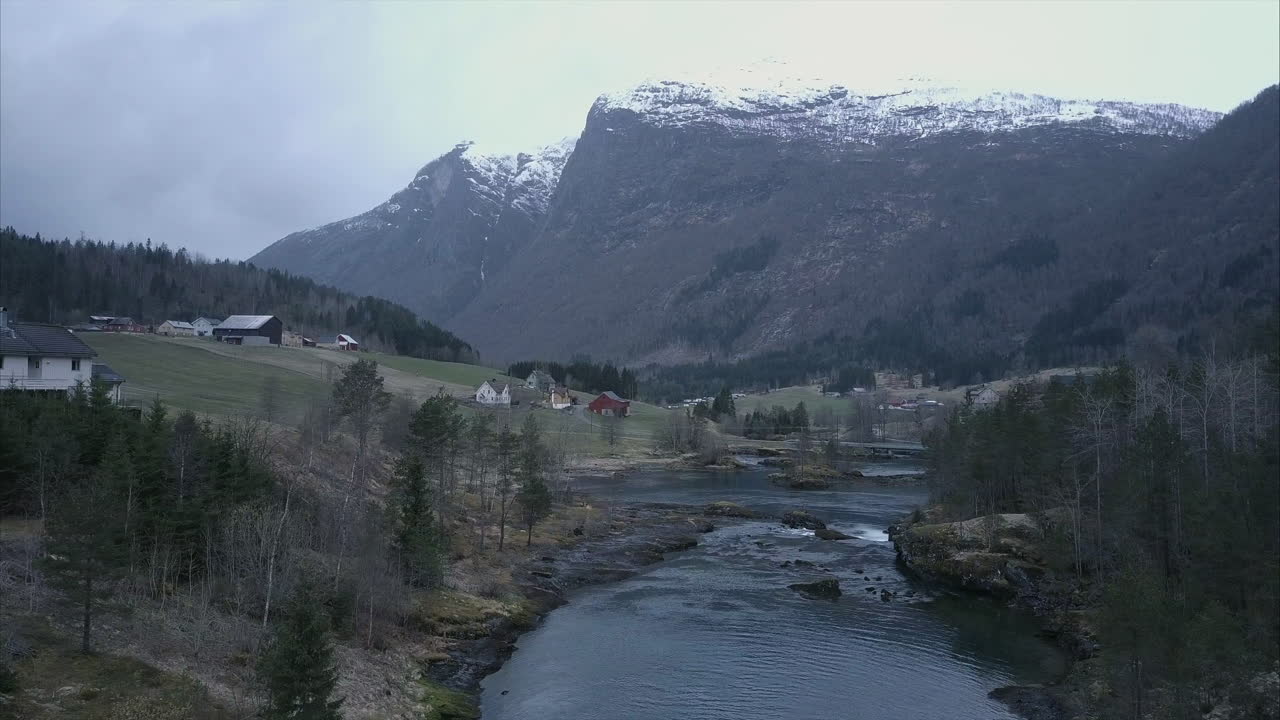 volando sobre el arroyo en el desierto noruego rodeado de montañas y casas, tiro aéreo