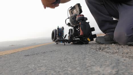 Videógrafo-Profesional-Ajustando-Su-Equipo-Y-Cámara-En-La-Lente-De-Cambio-De-Carretera-Asfaltada