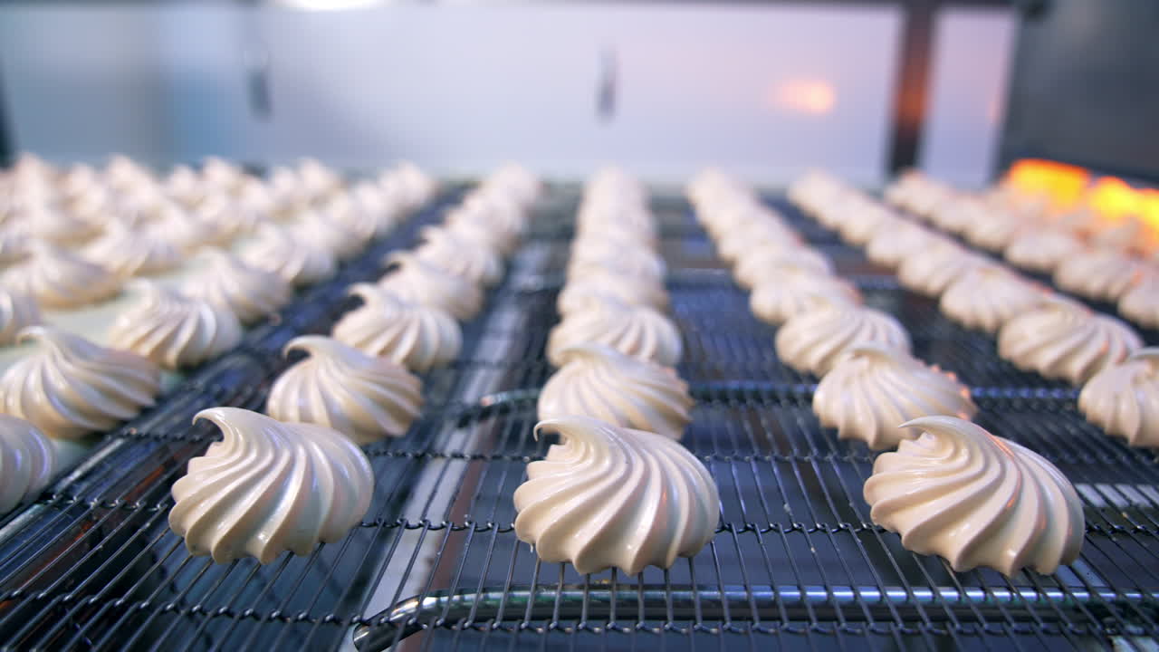 Tasty zephyr candies moving on the conveyor grid. Close up. Automated production of sweets at factory. Blurred background.