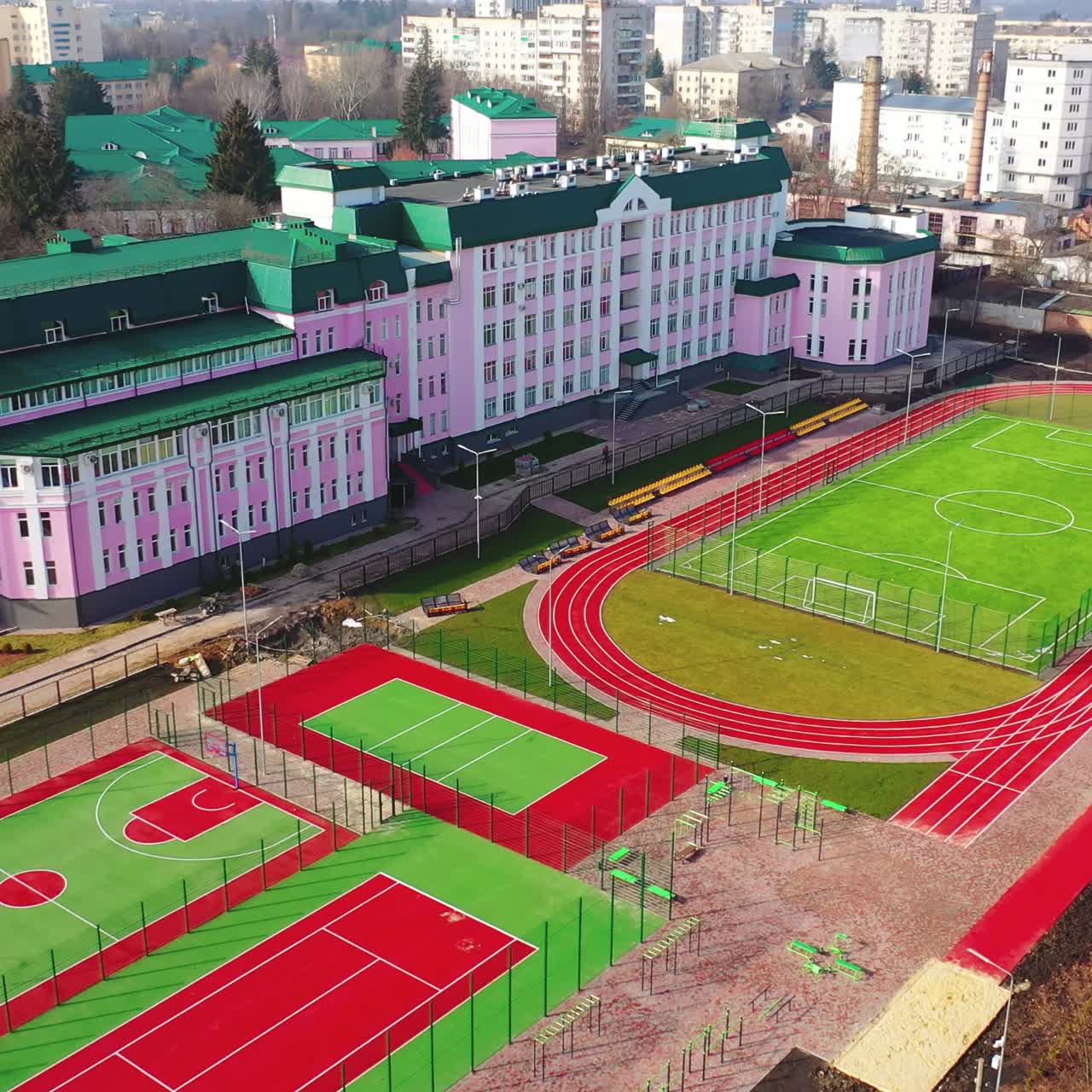 Green and red stadiums near the modern building. Modern outdoor fields for sports in the city. New basketball and football fields. Aerial view