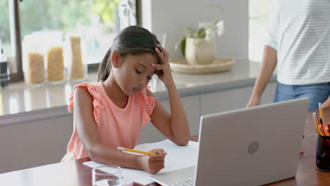 Feliz-Madre-Birracial-Ayudando-A-Su-Hija-A-Usar-Una-Computadora-Portátil-Para-Las-Tareas-Escolares-En-La-Cocina,-Cámara-Lenta