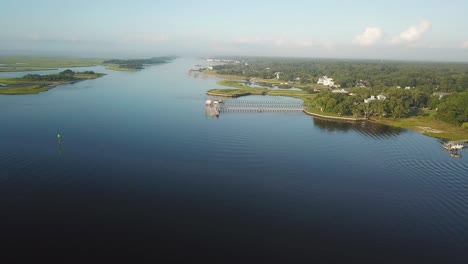 Peaceful-sunrise-pan-left-flyover-of-piers,-houses,-and-marsh-at-Trails-End-Park-in-Wilmington-North-Carolina