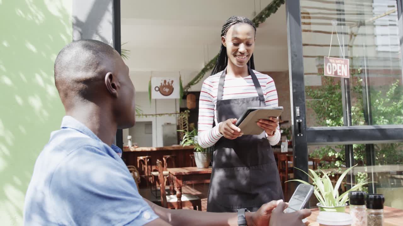 barista afroamericana con tableta tomando el pedido del cliente fuera de la cafetería, cámara lenta