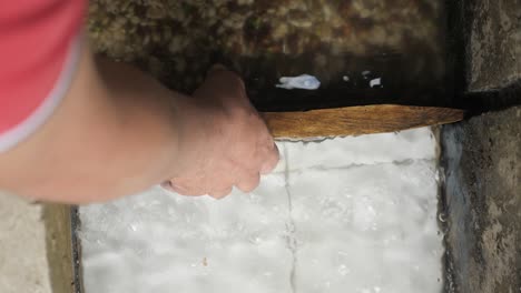 Shot-from-above-a-man-who-is-holding-a-small-wooden-dam-to-let-the-water-out-from-the-container-after-being-cleaned-with-water-on-coffee-beans-plantation-factory-Sierra-Nevada-Colombia-slowmotion