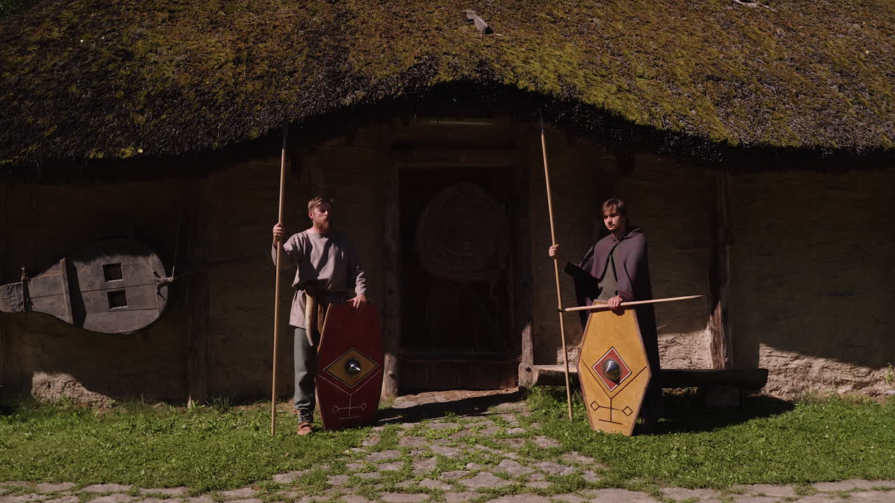 Two Warriors in Front of a Traditional Hut