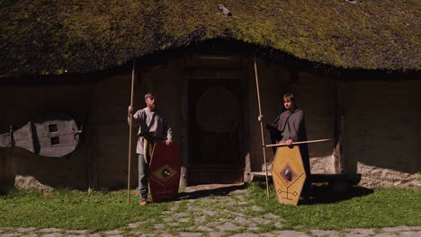 two warriors in front of a traditional hut