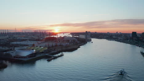 Aerial-dolly-out-view-of-a-boat-driving-along-Elbe-river-past-warehouses-in-industrial-district-of-Hamburg-port