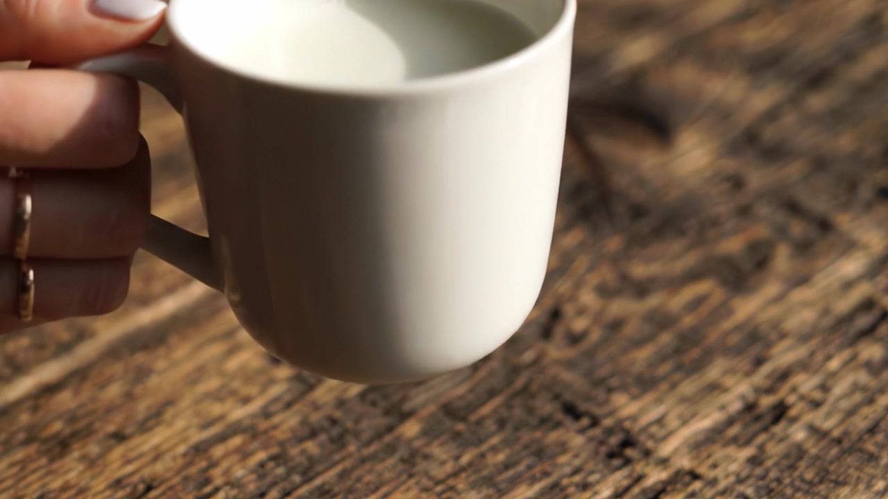 A close-up view of a hand gently holding a simple white mug filled with liquid, resting on a rustic wooden table, capturing a serene moment of quiet reflection.