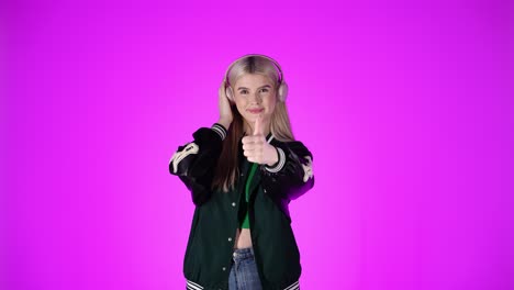joven rubia feliz baila a la música en los auriculares y muestra los pulgares hacia arriba
