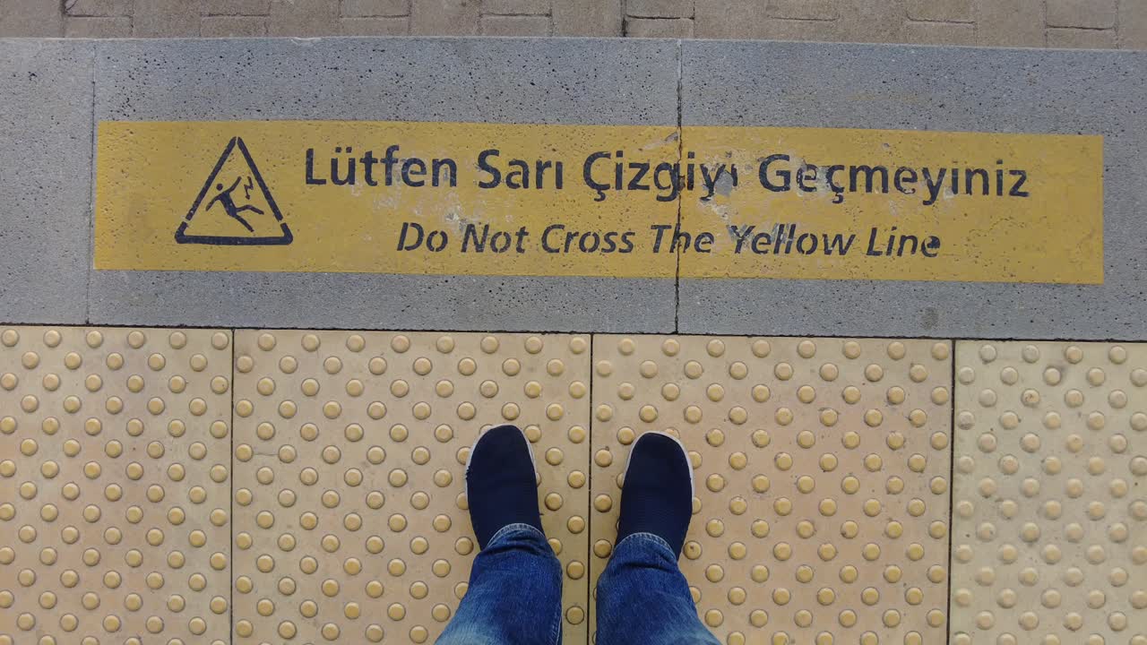 노란 선을 넘지 말라는 경고 표지판이 있는 기차역 플랫폼에 서 있는 사람.