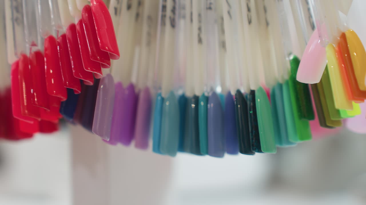 Close up view of vibrant nail polish samples hanging neatly on plastic sticks with a soft blur background, showcasing a variety of shades including red, purple, teal, and green in salon setting