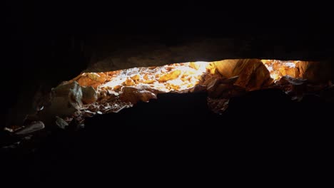 Tilting-up-shot-revealing-a-beautiful-golden-cave-entrance-with-the-bright-light-outside-in-the-Lapa-Doce-cave-in-the-Chapada-Diamantina-National-Park-in-Bahia,-northeastern-Brazil